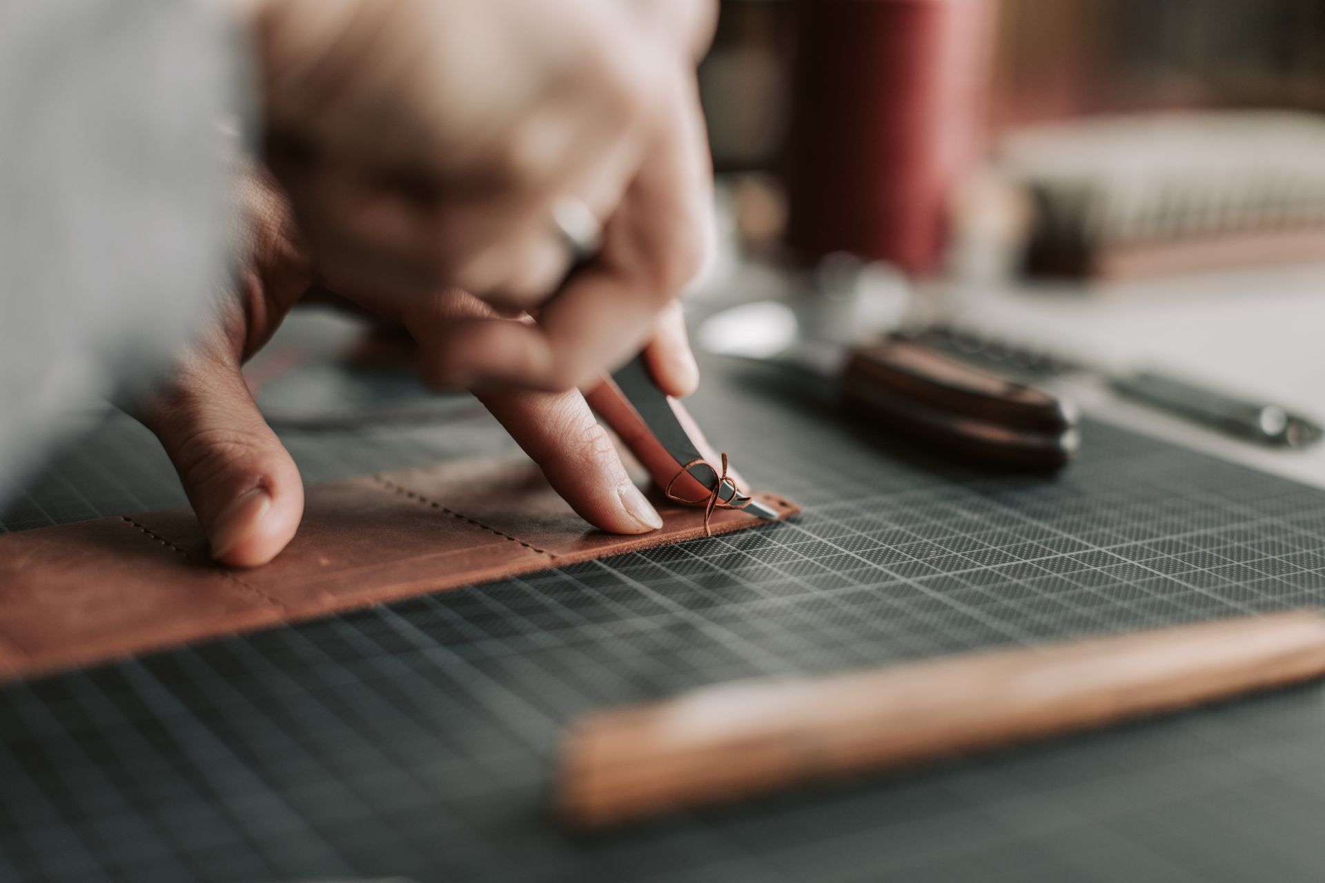 A hand cutting a strip of leather with a craft knife.